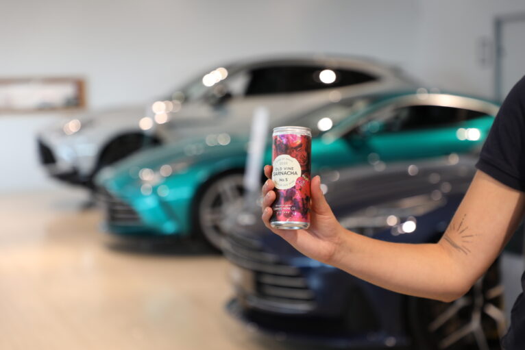 Canned Wine Co. Old Vine Garnacha held in front of Aston Martin cars